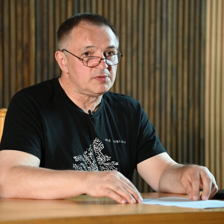 W czarnej koszulce Wojciech Birek siedzi za stołem w sali WDK podczas wykładu