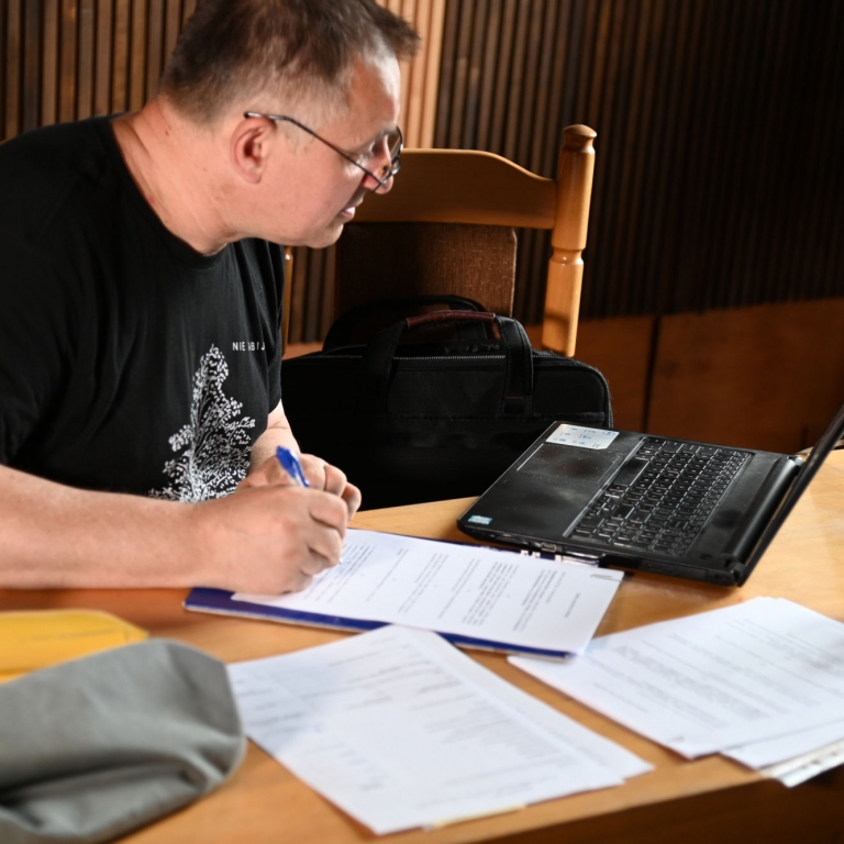 Wojciech Birek przy stole podpisuje dokumenty przed nim stoi na biurku laptop